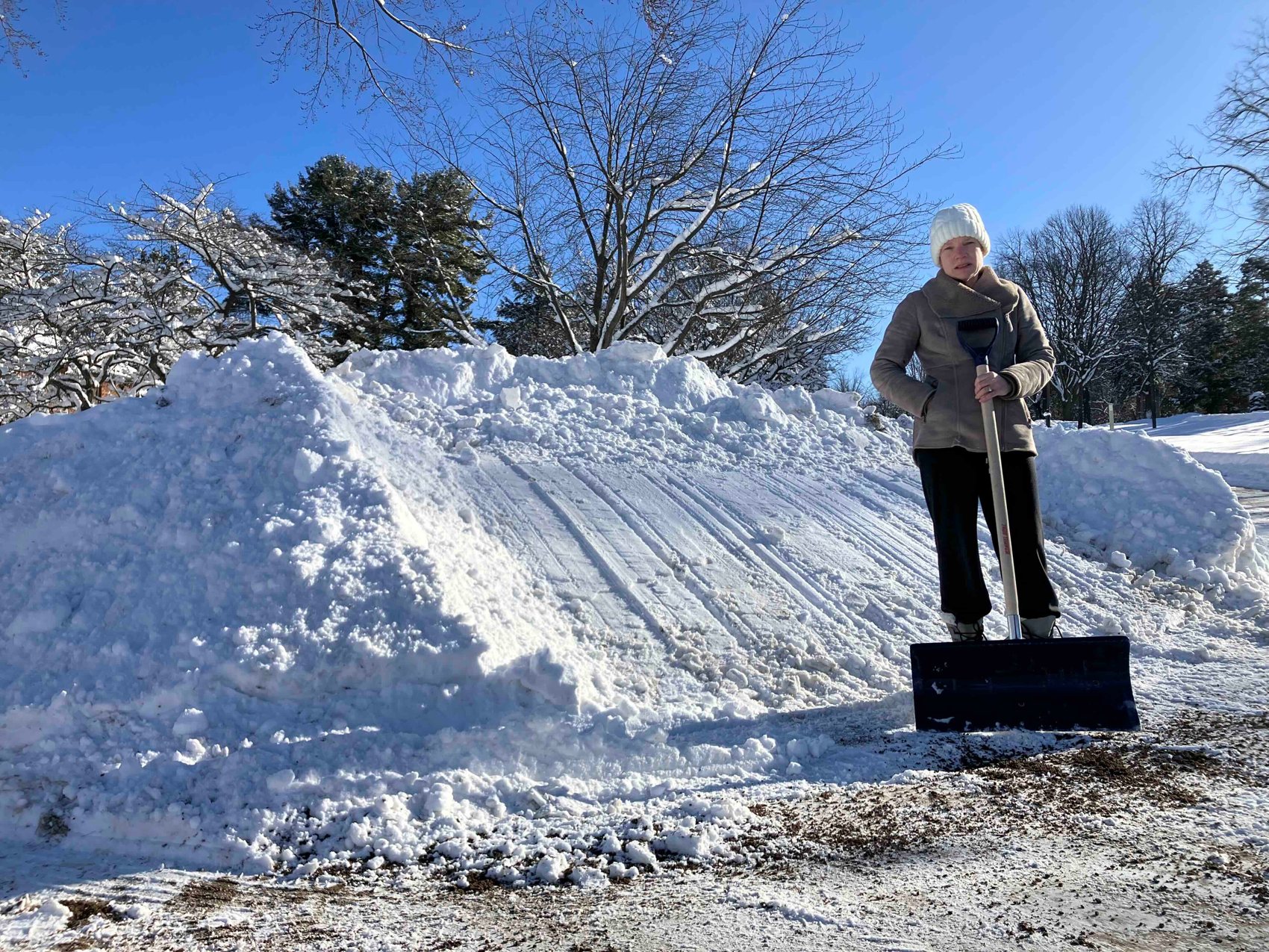 A neighbor standing beside a snowbank taller than she is at the end of a driveway
